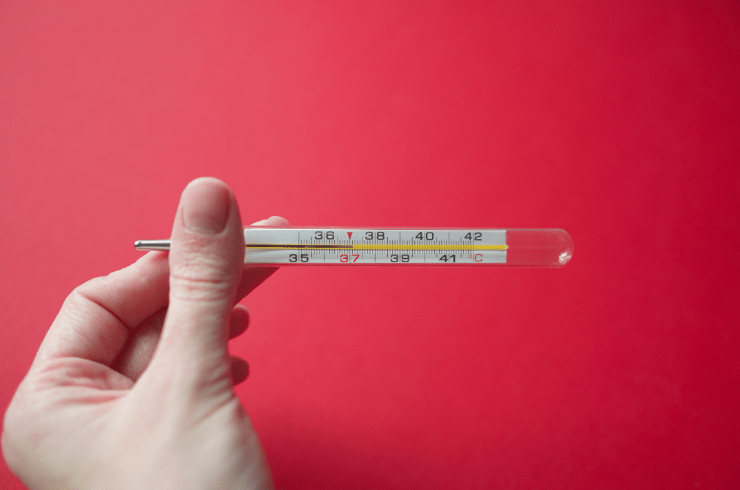 Hand holding clinical thermometer in front of eyes.