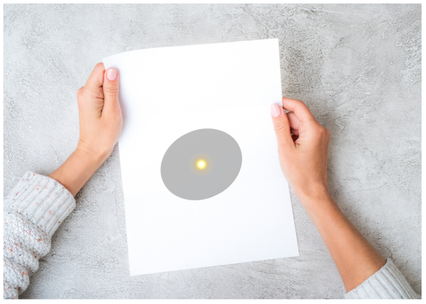 Round shadow on sheet of paper with bright yellow spot in the middle.
